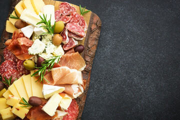 Antipasto. Cheese and meat - jamon, salami with olives at wooden serving board at black background....