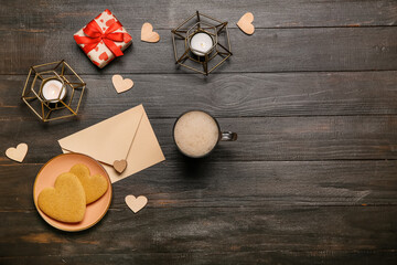 Cup of coffee, cookies, envelope, candles and gift on dark wooden background. Valentine's Day celebration