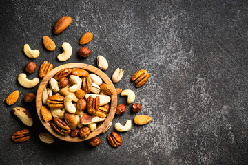 Assortment of nuts in wooden bowl on dark stone table. Cashew, hazelnuts, almonds, brazilian nuts and pecans. Top view with copy space.
