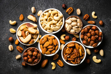Assortment of nuts in bowls. Cashew, hazelnuts, pecan, almonds, brazilian nuts and pistachios. Top view with at black stone table.