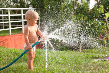 Child toddler boy playing with water hose outdoors in summer, summer activities 