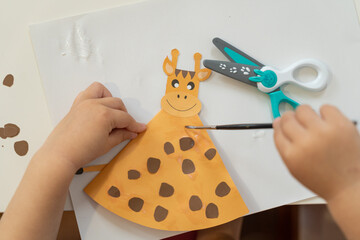small child glues a giraffe from colored paper	
