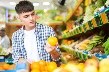 Portrait of young male choosing fresh oranges in fruit store