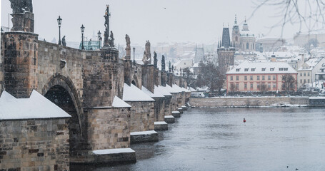 Prague in the snowfall. View of the Charles Bridge and the Vltava River on a winter day. Czechia