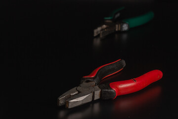 Fototapeta premium Pliers Open metal nippers with a red and green handle isolated on black background