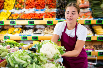 Portrait of joyful female merchandiser with cauliflower in hands at grocery supermarket