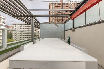 Community penthouse terrace of an urban residential building with dining tables with white Teflon tops and metal structures with retractable awnings