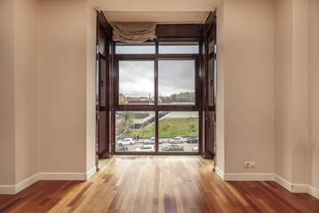 empty living room of a house with wooden floors, gathered curtains and a glass window overlooking a dark day with clouds