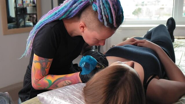 Tattoo artist girl at work.A feminist with dreadlocks gets a tattoo.A strong woman gets a tattoo.Close-up.Slow motion.The master fills a beautiful abstract tattoo. Concept of gender expression. LGBTQ+