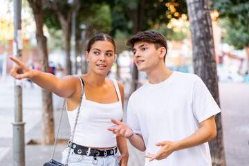 Obraz premium Young positive tourist couple walking around foreign city on summer day, pointing at sights