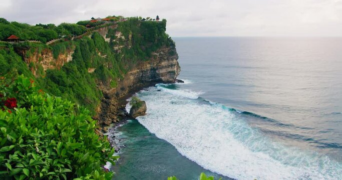 Ocean view with ancient Pura Luhur Uluwatu Temple Bali Isalnd Indonesia. Huge cliff with exotic plants against blue Indian waters. Famous historic monument.