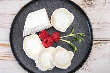 French organic matured white goat cheese with white rind close up served with fresh raspberries