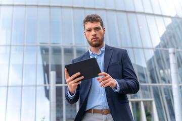 Fototapeta premium Young male entrepreneur outside the office, walking around with a tablet in his hand
