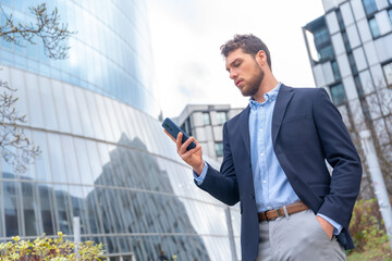 Male businessman or entrepreneur looking at mobile outside the office, business park
