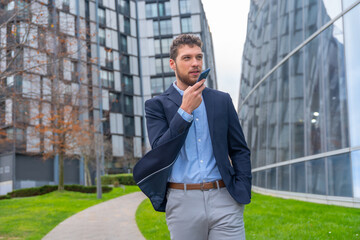 Businessman or finance man sending a voice note with the phone outside the office, business park
