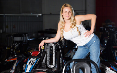 happy blonde woman playfully posing near cars for karting in sport club