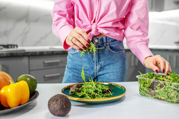 Woman is preparing salad from vegetables and spring mix in kitchen. Concept of healthy food. Closeup