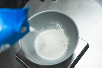 Top view of white sugar being poured intro a bowl placed on a metal stand. Blurred foreground. High quality photo