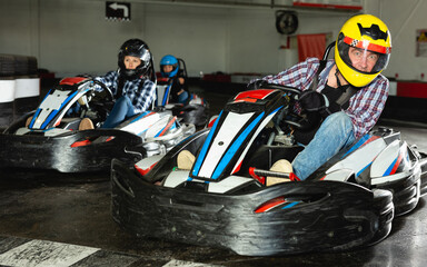 Young positive people in helmets driving go-kart cars in sport club