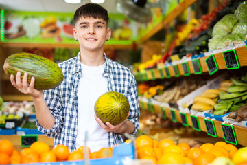 Young male consumer in plaid shirt picking ripe melon during shopping in hypermarket