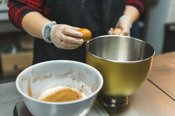 Unrecognizable caucasian pastry chef cracking an egg on the brim of a stainless steel mixing bowl. Cupcake recipe. High quality photo