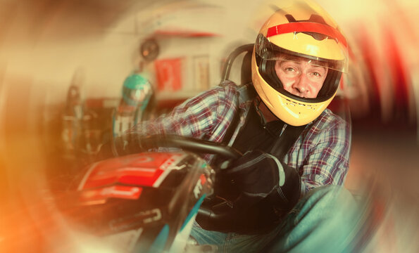 Portrait of happy cheerful smiling male racer in helmet driving kart on track