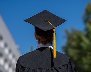 Rear view of caucasian woman in graduate gown near university. 