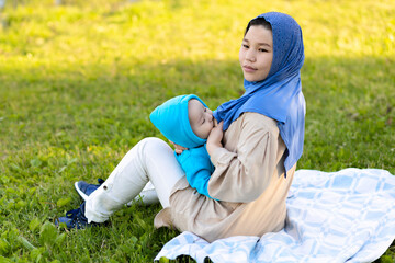 breast feeding concept. young islamic woman hugging newborn baby boy in park. asian mother in hijab breastfeeding baby outdoors