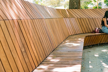 A long wooden bench in the city park. Elegant. Contemporary. Colourful. Life. Massive. Tranquil. Idyllic. Restful. Quiet. Calm. Leisure. Relaxing. Elderly. Wooden. Gardening. Material