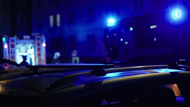 Defocused view over TWO large firefighters trucks. Night city illuminated by emergency siren lights