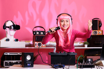 Asian musician sitting at dj table performing techno music using professional turntables, wearing...