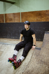 Young skater in rollers sitting on ramp in skate park 