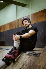 Athletic roller skater in helmet resting on ramp in skate park 