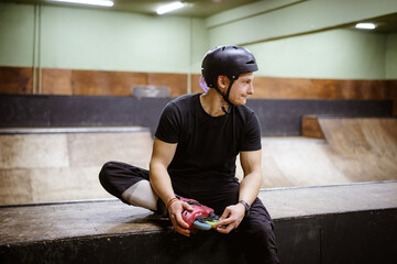 Smiling roller skater in helmet sitting on ramp in skate park 