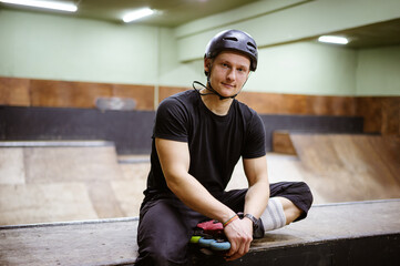 Young man in roller blade and helmet looking at camera on ramp in blurred skate park 