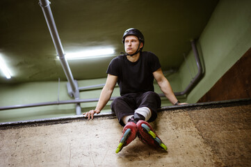 Low angle view of tired man in rollers and helmet sitting on ramp 