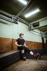 Roller in skates and helmet looking away while sitting on ramp 