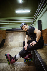 Man in rollers and helmet looking at camera while sitting on ramp at rollerdrome 