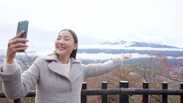 Asian woman enjoy outdoor lifestyle travel Japan on autumn holiday vacation. Attractive girl using mobile phone taking selfie while travel around Mt.Fuji with beautiful red maple tree leaves falling.