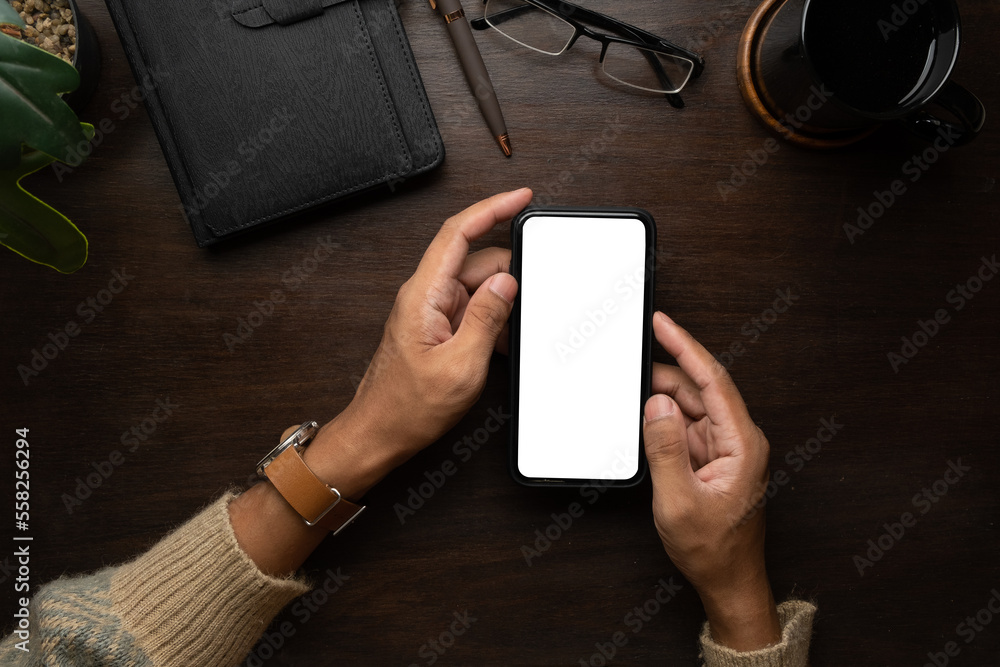 Poster above view of man in warm sweater using smart phone on wooden working table.