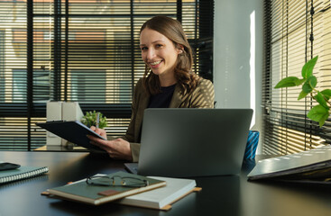 Beautiful caucasian female manager using laptop computer and working financial document at her workstation.