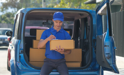 Portrait of a delivery man in blue uniform checking delivery list while sitting among packages in back of van.