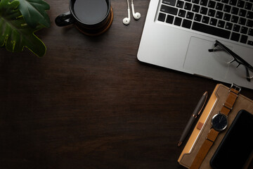 Simple workspace with laptop, coffee cup, glasses and wrist watch on wooden table.