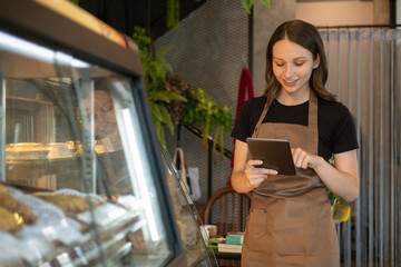 Smiling caucusian woman entrepreneur using digital tablet while standing in front of the counter in cozy coffee shop interior.