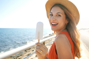 Close-up of laughing Brazilian woman eating a lemon popsicle looking at the camera on summer
