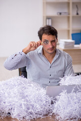 Young male employee and a lot of cut papers in the office