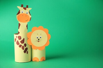 Toy giraffe and lion made from toilet paper hubs on green background, space for text. Children's handmade ideas
