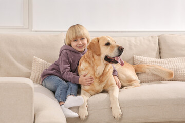 Cute little child with Golden Retriever on sofa at home. Adorable pet