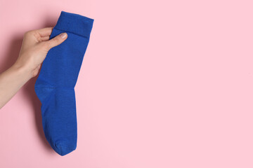 Woman holding blue sock on light pink background, closeup. Space for text