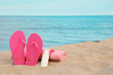 Fototapeta na wymiar Beach towel, slippers and sunscreen on sand near sea, space for text